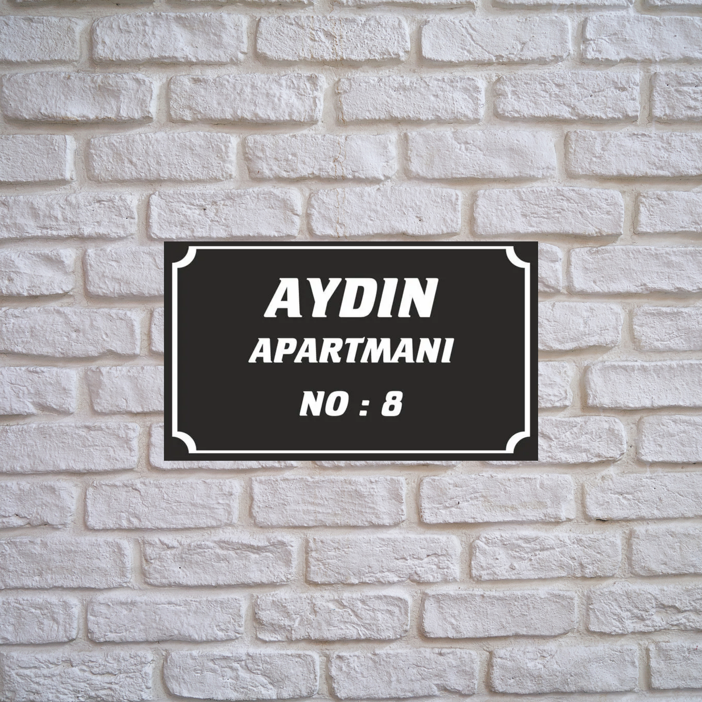 Kişiye özel apartman adı ve numara yazılı siyah pleksi tabela, beyaz tuğla duvar üzerinde lifestyle görseli