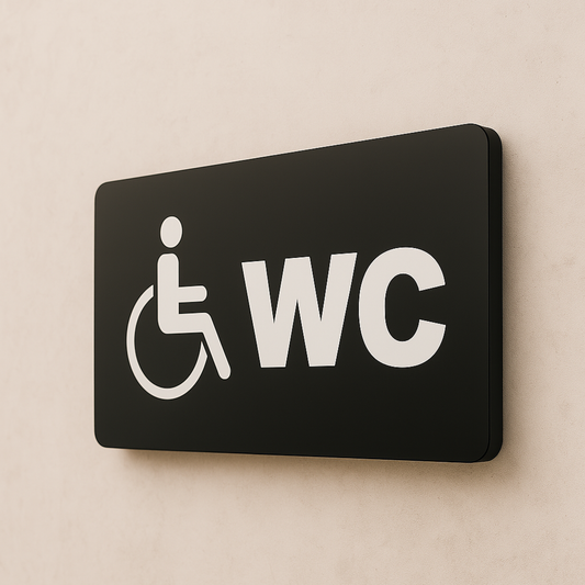 Engelli WC tabelası, siyah metal yüzey, tekerlekli sandalye ikonu ve WC yazısı, 22x8 cm